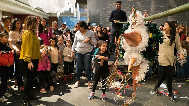 a crowd watches a young girl try to hit a piñata