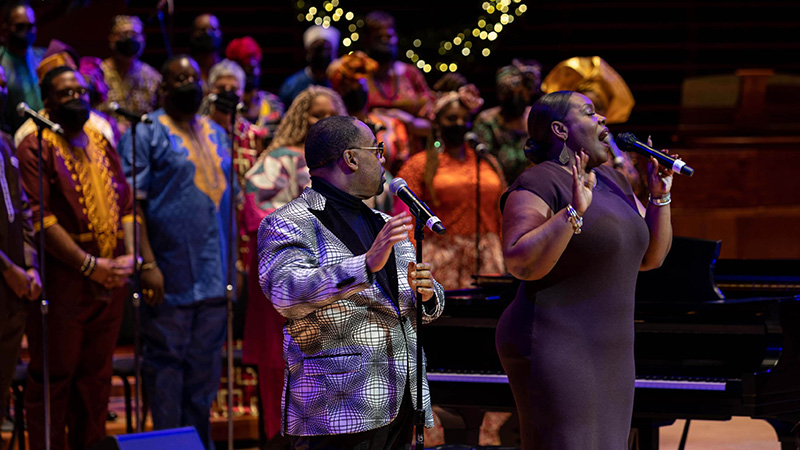 Two singers in front of a choir performing on stage for A Soulful Christmas 
