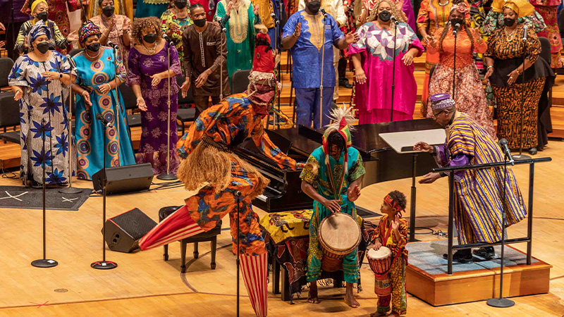 Musicians playing the drums and dancing in front of a choir on stage