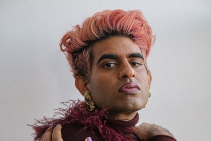 A non-binary person with pink hair in a feathery turtle neck posing for a headshot
