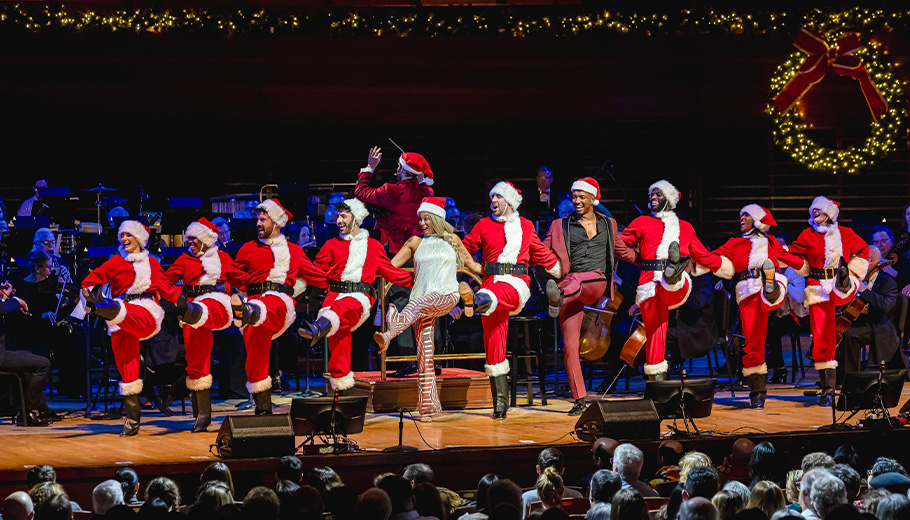 A Very Philly Christmas performers dressed as Santa dancing in a kick line on stage.