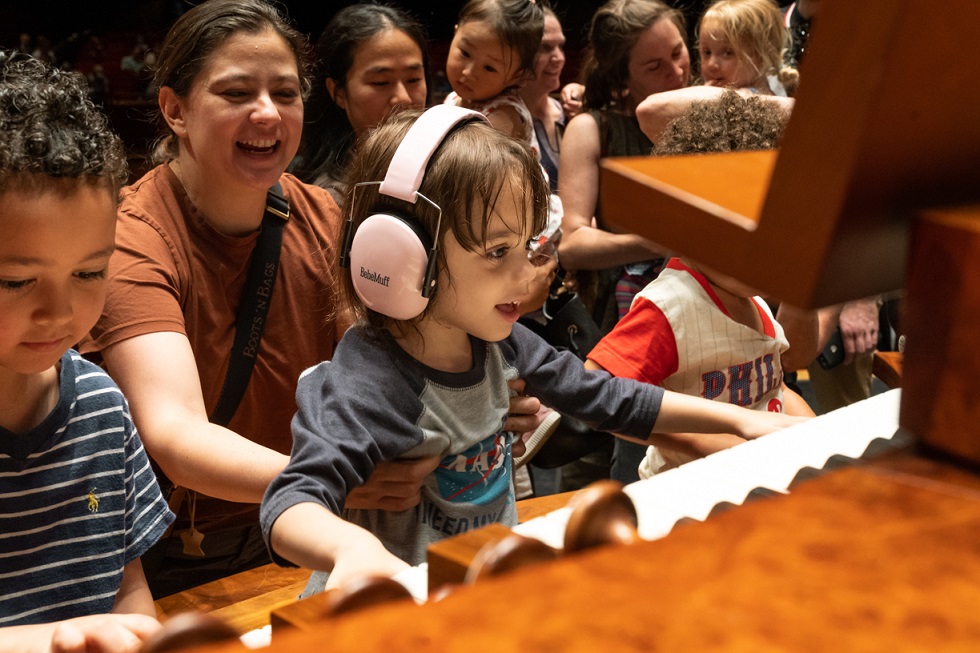A small child with headphones on sits at the keys of the Fred J. Cooper Memorial Organ on the Kimmel Cultural Campus during a free event 