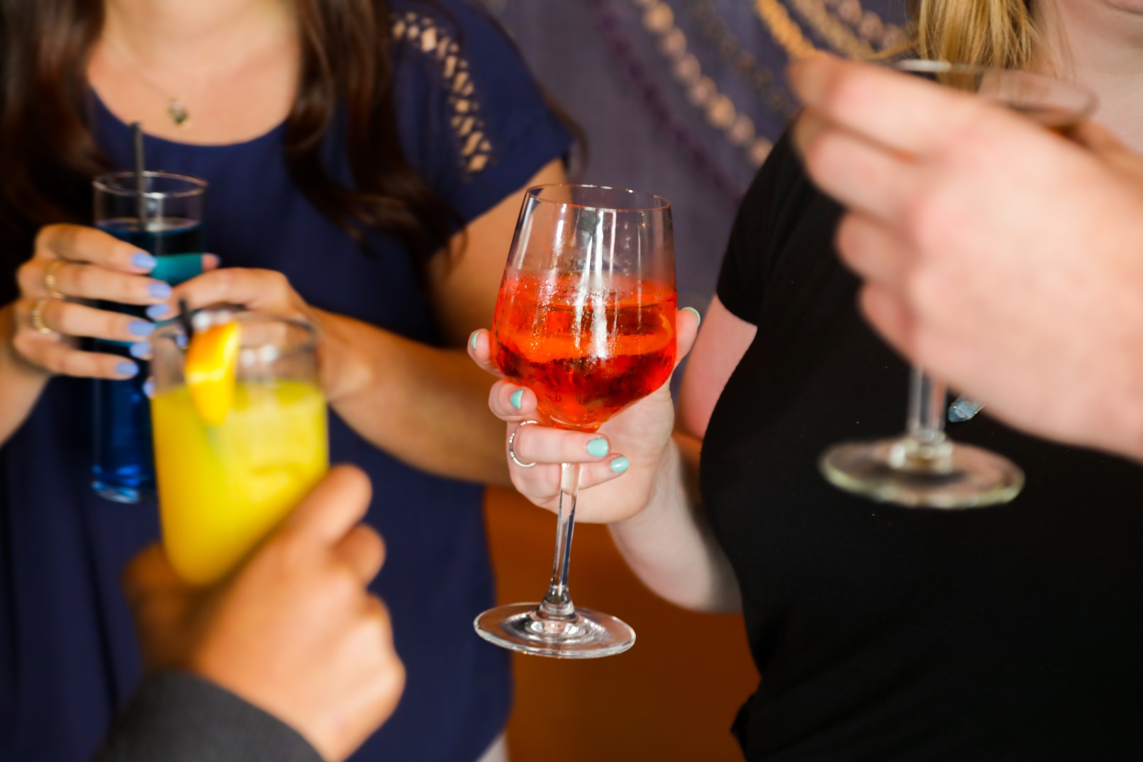 A hand holding a red cocktail in a wine glass surrounded by other people holding cocktails