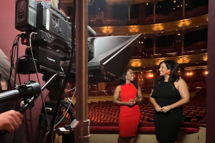 Two reporters in front of a film camera in the Academy of Music