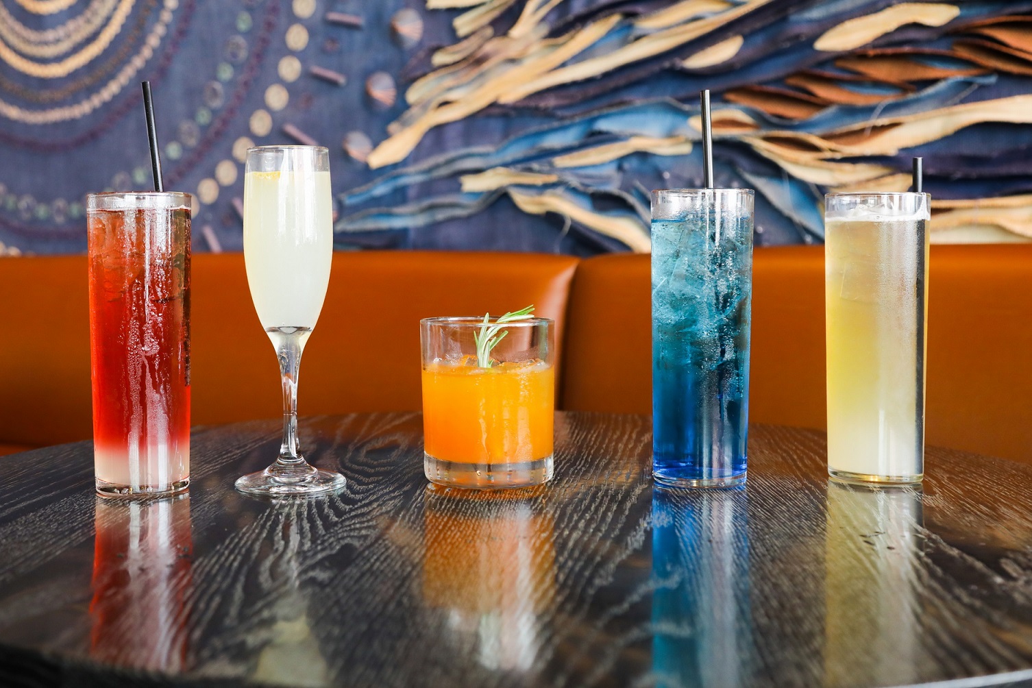 A row of colorful mixed drink cocktails in varying glasses sit on a table