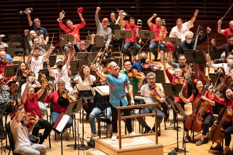 Yannick Nézet-Séguin and the Philadelphia Orchestra pose on stage in Philadelphia Phillies gear after playing an orchestral arrangement of Robyn's "Dancing On My Own"
