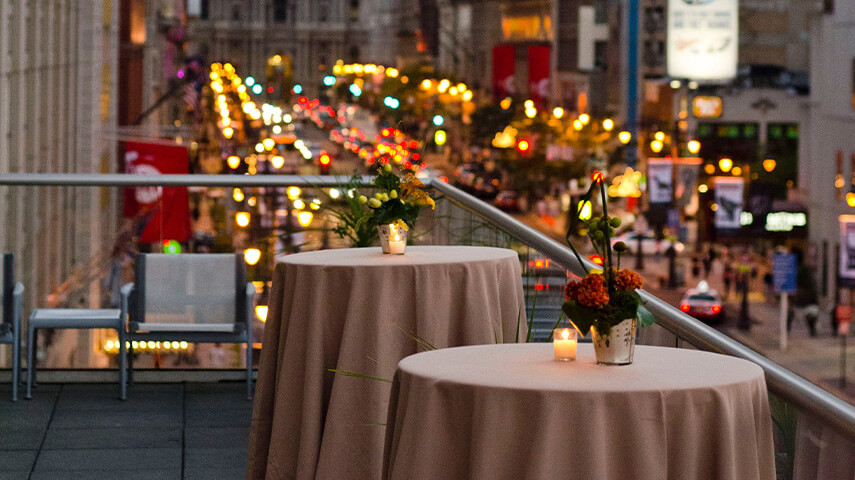 Tables set with tablecloths and flower centerpieces outside on the terrace.