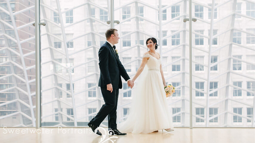 A bride and groom holding hands while walking through The Kimmel Center.